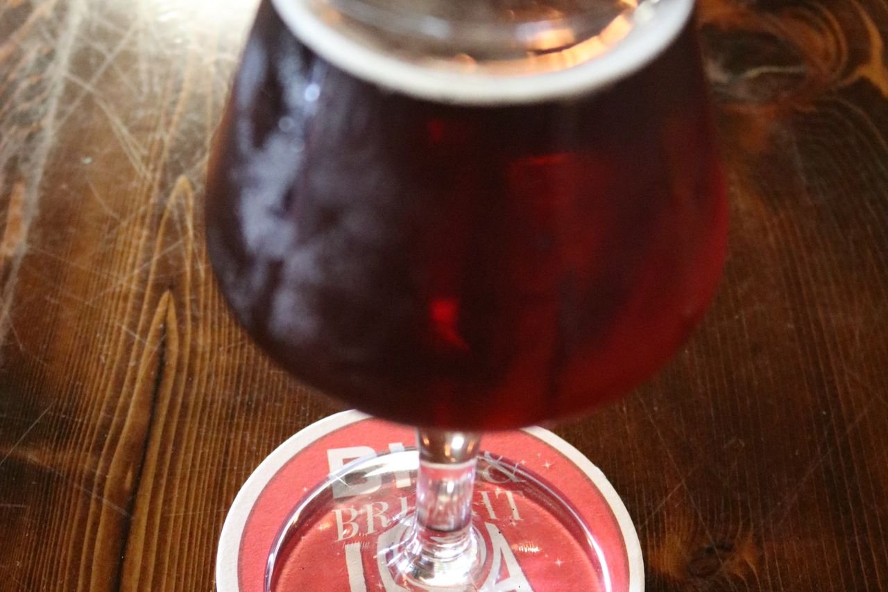 Two contrasting IPA glasses on a wooden bar coaster — one hazy and opaque, one crystal clear and golden