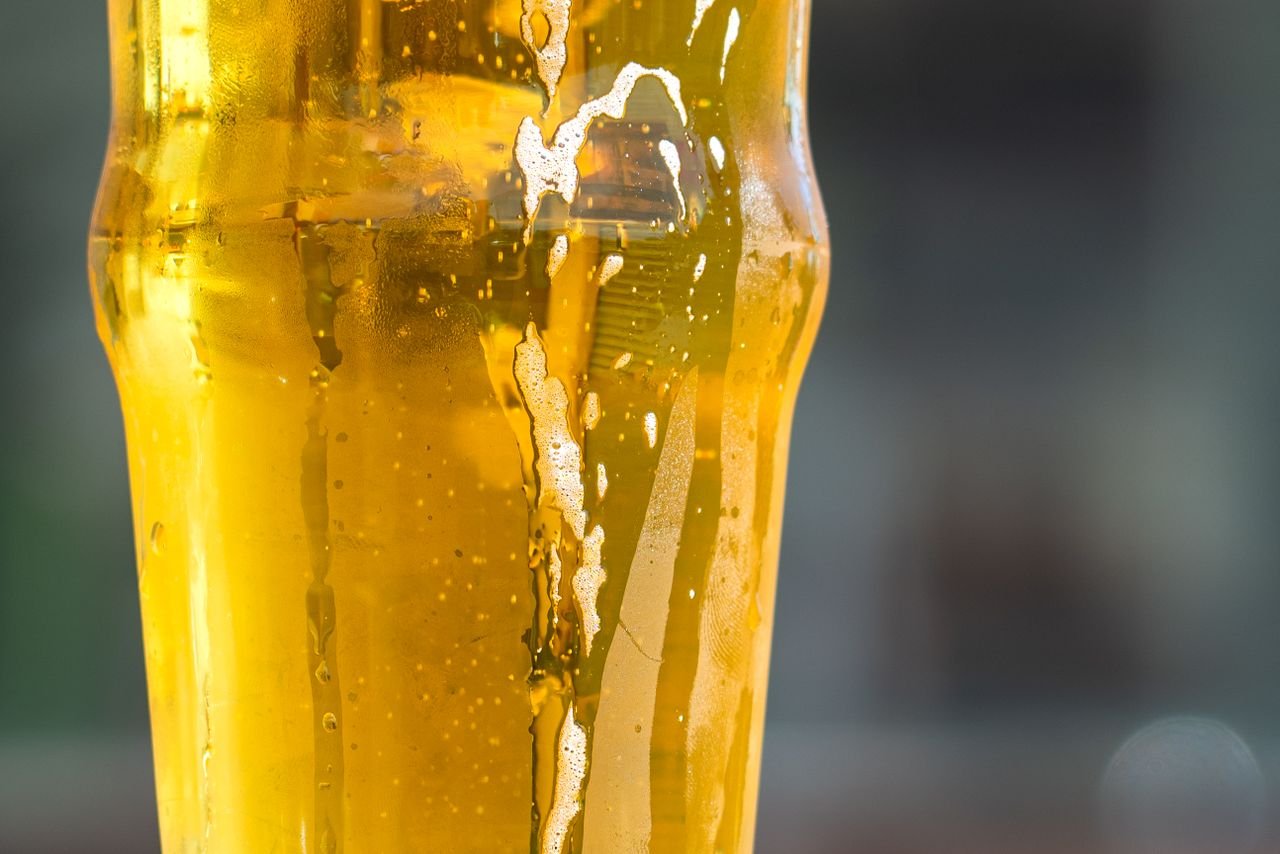 A refreshing golden beer with hops visible in the background and condensation on the glass