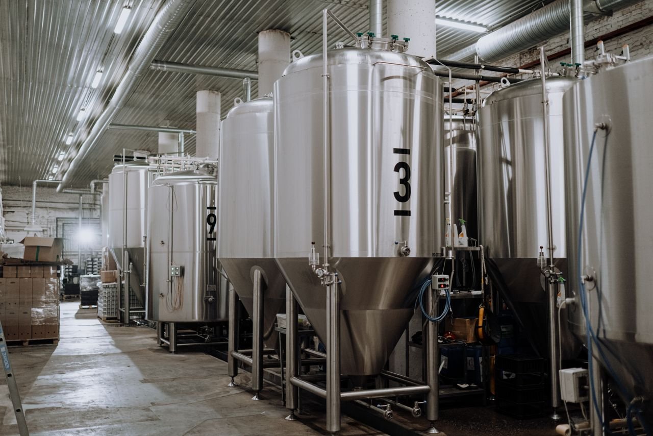 Interior of a craft brewery with rows of bright copper and stainless tanks under warm lighting