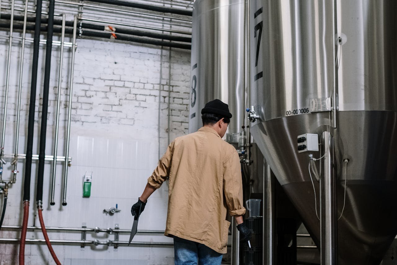 Brewery worker taking notes beside large stainless fermentation tanks