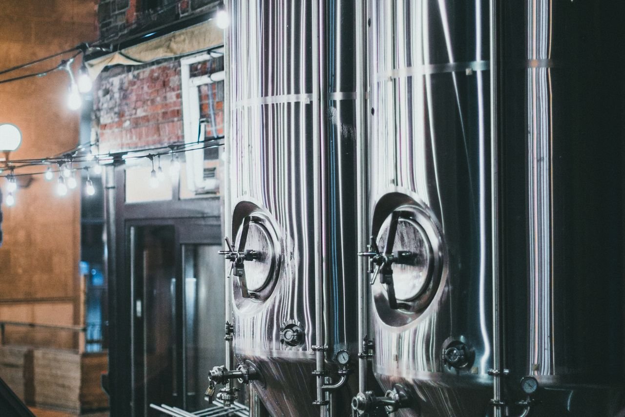 Large cylindroconical fermentation tanks illuminated against a dark brewery at night
