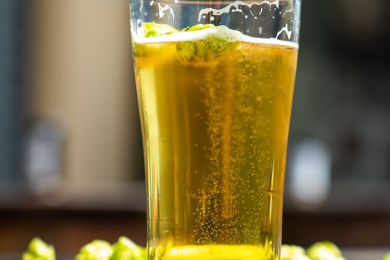 Glass of golden craft beer surrounded by fresh hop cones and loose hops on a wooden surface