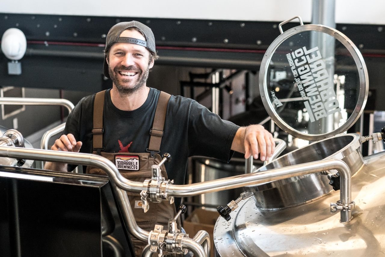 Smiling homebrewer holding a glass of freshly poured amber ale in their home brewery