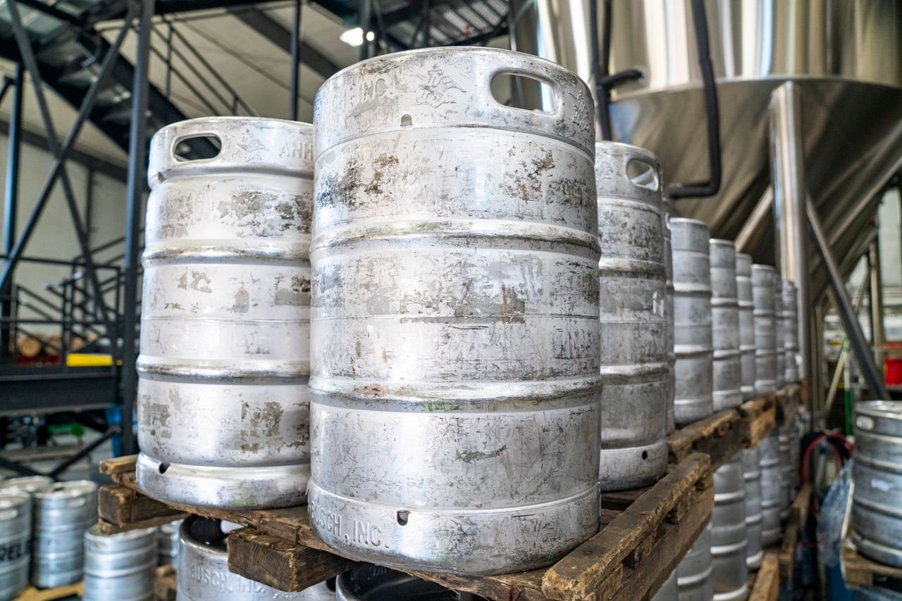 Stacked kegs on pallets in a brewery warehouse, representing the scale of grain-to-glass brewing