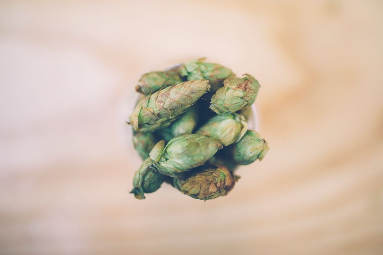 A small ceramic cup filled with dried hop pellets on a wooden surface