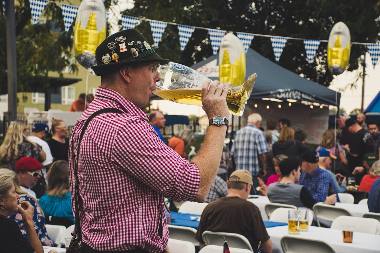 Smiling man in traditional dress lifting a huge beer mug at an outdoor festival