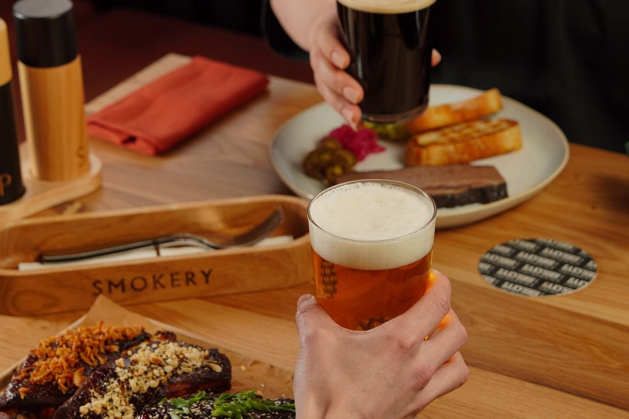 A plate of pub ribs next to a pint of dark beer on a worn wooden table